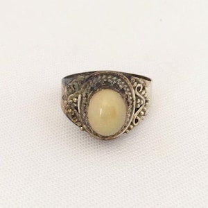May include: A silver ring with an oval-shaped white stone set in a filigree design.