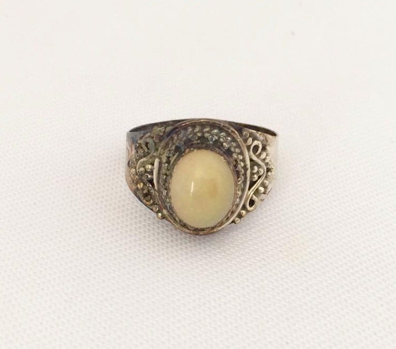 May include: A silver ring with an oval-shaped white stone set in a filigree design.