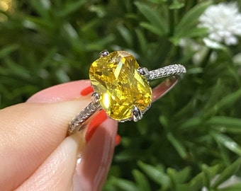 May include: A silver ring with a large, oval-shaped, yellow gemstone. The ring has a delicate band with small, clear stones.