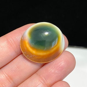 May include: A round, green, white, and orange gemstone with a swirling pattern. The gemstone is polished and has a smooth surface.