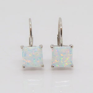 May include: A pair of silver earrings with white opal square stones. The earrings have a lever back closure.