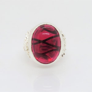 May include: A silver ring with a large oval-shaped red gemstone. The gemstone has a black swirl design.