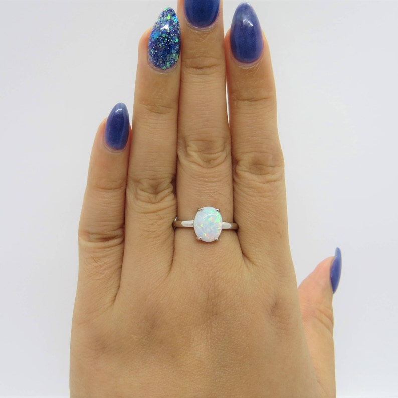 Peut inclure: Une bague en argent avec une pierre d'opale blanche. La bague est port&eacute;e sur un doigt.