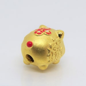 May include: A gold-colored ceramic pig figurine with red accents. The pig has a hole in the back, suggesting it may be a piggy bank or a charm.