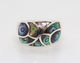 May include: A silver ring with a mosaic design featuring iridescent abalone shell pieces in shades of blue, green, and purple. The ring has a wide band and a polished finish, showcasing the natural beauty of the shell.