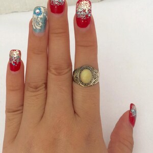 May include: A silver ring with an oval-shaped, light yellow gemstone set in a filigree design.
