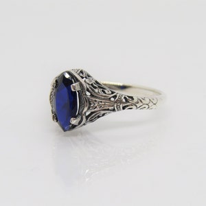 May include: A silver ring with an intricate filigree design and a large, oval-shaped blue gemstone.