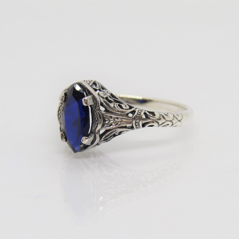 May include: A silver ring with an intricate filigree design and a large, oval-shaped blue gemstone.