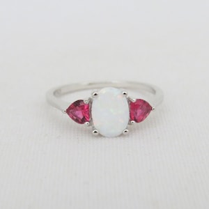 May include: A silver ring with a white oval opal gemstone and two pink heart-shaped gemstones.