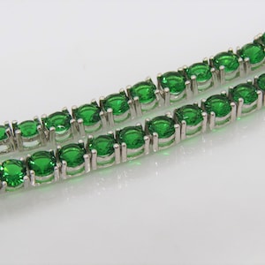 May include: A silver tennis chain bracelet with green round gemstones.