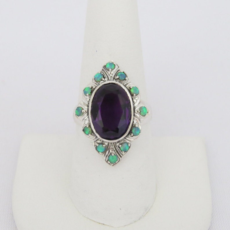May include: A silver ring with a large oval amethyst gemstone surrounded by smaller green opal gemstones.
