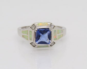 Può includere: Un anello d'argento con una pietra preziosa quadrata blu circondata da pietre di opale bianco e zircone cubico trasparente.