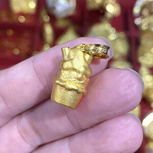May include: A gold-colored pendant in the shape of an ice cream cone. The pendant has a textured surface and a small loop at the top for a chain. The loop is stamped with the number "9999".