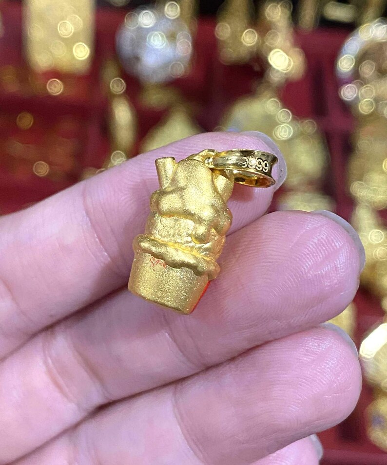 May include: A gold-colored pendant in the shape of an ice cream cone. The pendant has a textured surface and a small loop at the top for a chain. The loop is stamped with the number "9999".