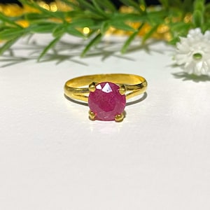 May include: A gold ring with a large, round, red ruby gemstone.