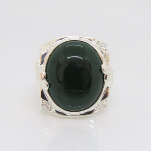 May include: A silver ring with a large, oval-shaped green gemstone set in a decorative silver setting. The ring has small, clear stones around the gemstone.