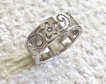 Puede incluir: Un anillo de banda de plata con un intrincado diseño floral. El anillo es ancho y tiene un acabado pulido.