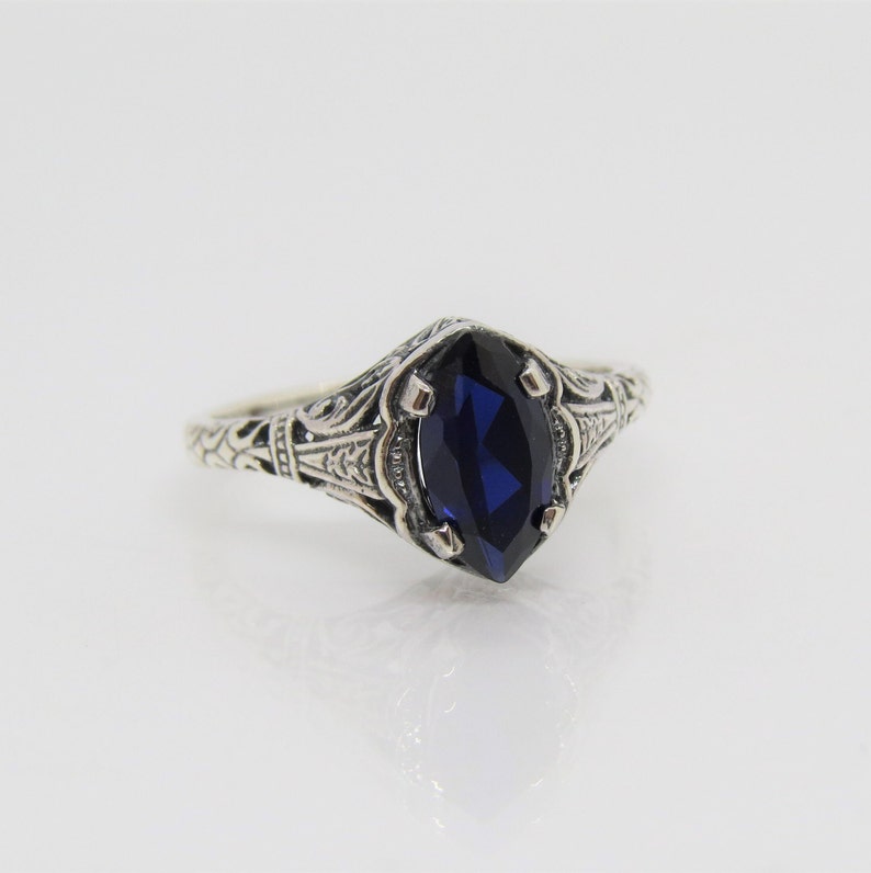 May include: A silver ring with an ornate filigree design and a dark blue marquise-shaped gemstone.