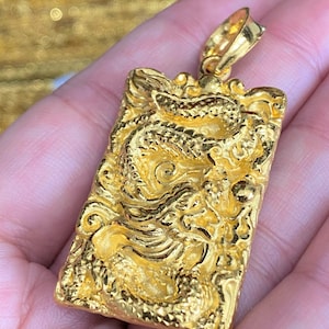 Pu&ograve; includere: Un ciondolo dorato con un designo di drago dettagliato. Il ciondolo &egrave; di forma rettangolare e ha una superficie testurizzata.