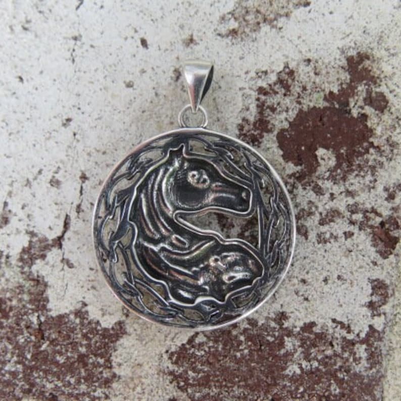 May include: Silver pendant featuring a detailed horse head design within a circular frame. The horse's head is facing right and the frame is decorated with a vine-like pattern.