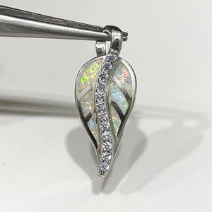 May include: A silver pendant shaped like a leaf with a white opal inlay and a row of clear cubic zirconia stones.