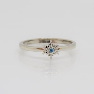 May include: A silver ring with a snowflake design featuring a small blue gemstone in the center.