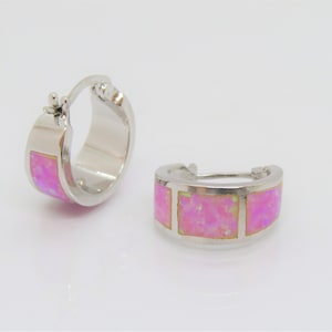 May include: A pair of silver hoop earrings with pink opal inlay. The earrings are approximately 1 inch in diameter.