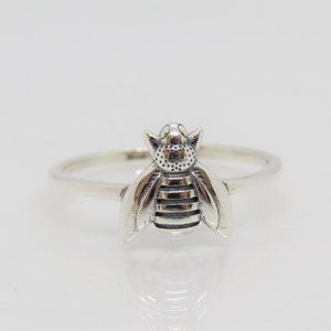 Può includere: Un anello d'argento con un design a forma di ape. L'ape è dettagliata con strisce e punti.