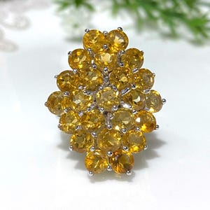 May include: A silver ring with a cluster of yellow citrine gemstones. The stones are set in a flower-like design.