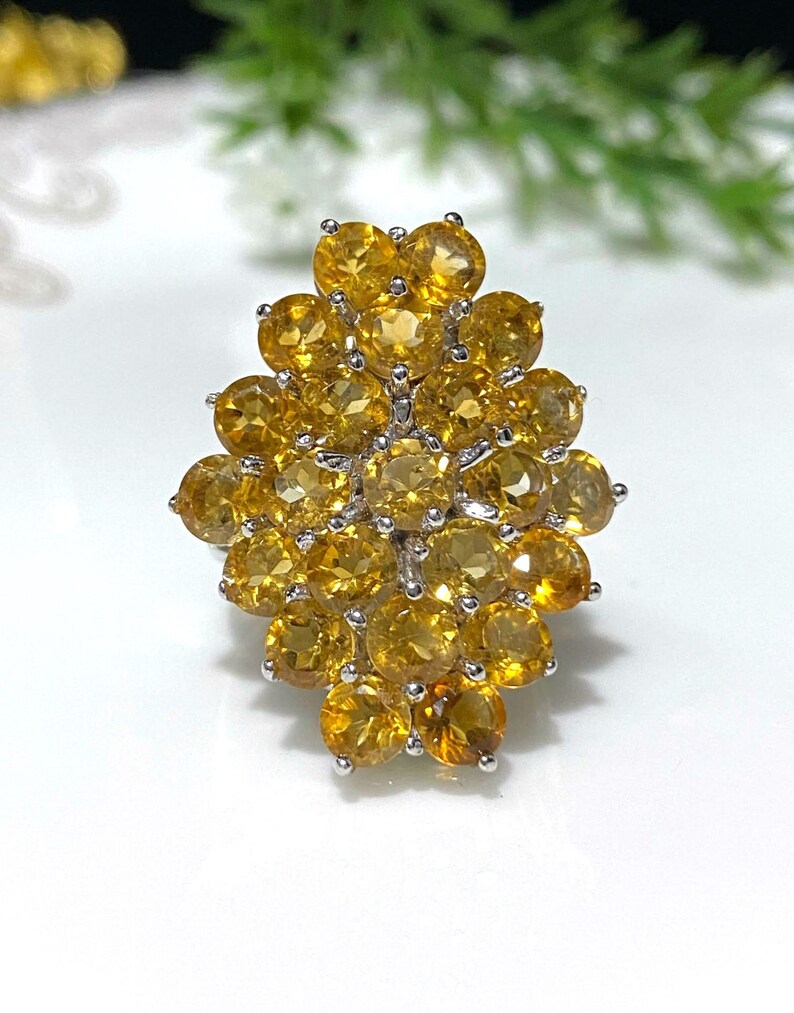 May include: A silver ring with a cluster of yellow citrine gemstones. The stones are set in a flower-like design.