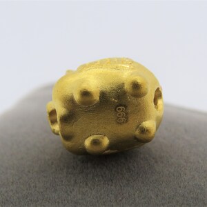 May include: A gold-colored, round, decorative object with a textured surface and a small hole on the side. The object has the number "666" stamped on the bottom.