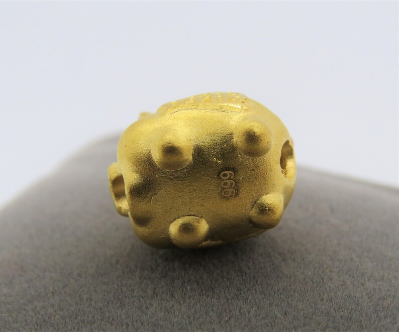 May include: A gold-colored, round, decorative object with a textured surface and a small hole on the side. The object has the number "666" stamped on the bottom.