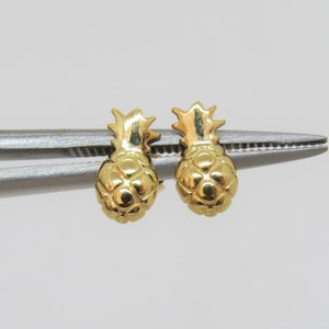 Puede incluir: Un par de pendientes de piña de oro. Los pendientes son pequeños y delicados, y son perfectos para añadir un toque de fantasía a cualquier atuendo.