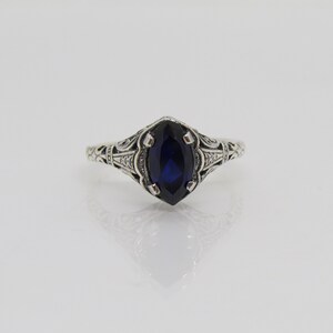 May include: A silver ring with an ornate filigree design and a dark blue marquise-shaped gemstone.
