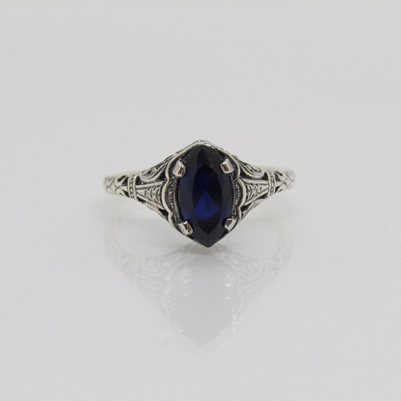 May include: A silver ring with an ornate filigree design and a dark blue marquise-shaped gemstone.