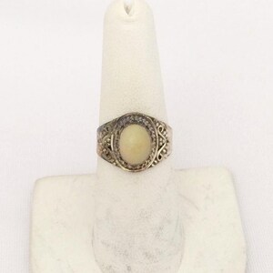 May include: A silver ring with an oval-shaped white stone set in a filigree design.
