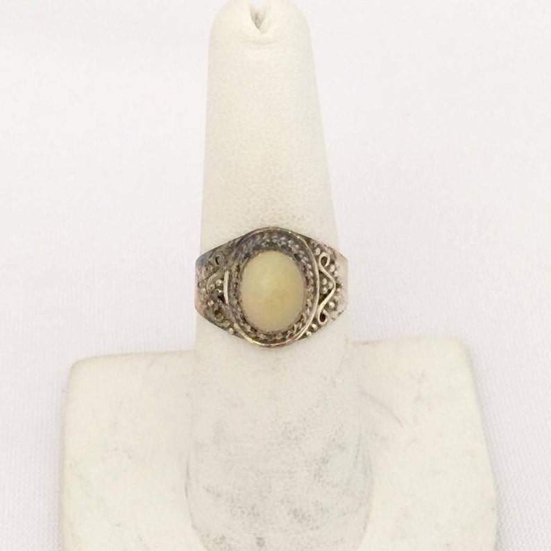 May include: A silver ring with an oval-shaped white stone set in a filigree design.