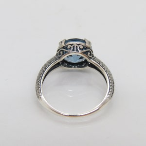 May include: A silver ring featuring a blue gemstone set within a filigree design. The band is textured with a repeating pattern.