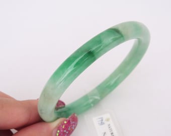 Könnte beinhalten: Ein grünes Jade-Armband mit weißem Innenleben. Das Armband ist glatt und poliert.