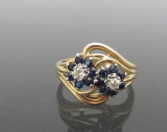 May include: A gold ring with two flower-shaped clusters of blue sapphires and white diamonds.