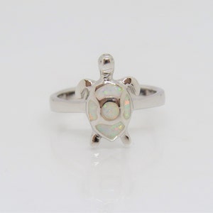 Puede incluir: Un anillo de plata con un diseño de tortuga de ópalo blanco.