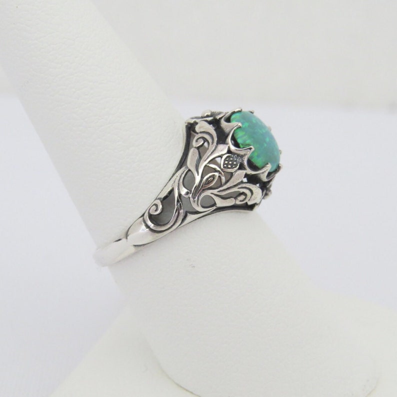 Pode incluir: Um anel de prata com uma pedra oval de opala verde engastada em um design filigranado.