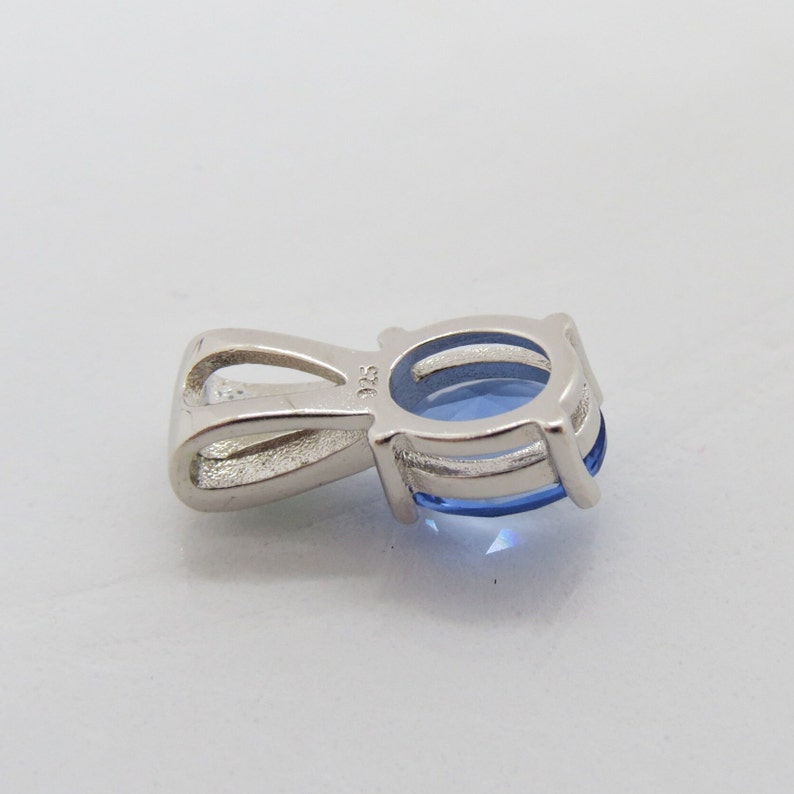 Op de afbeelding: Een zilveren hanger met een lichtblauwe ovale edelsteen. De hanger heeft een lus voor een ketting en is gezet in een vier-klauwzetting. Het metaal is gestempeld met "925".