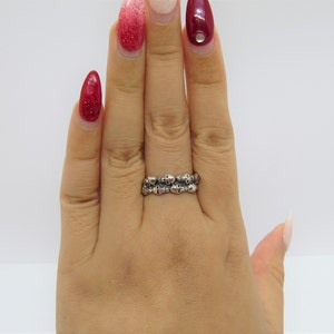 May include: A silver ring with a double row of skull designs. The ring is worn on a person's finger.