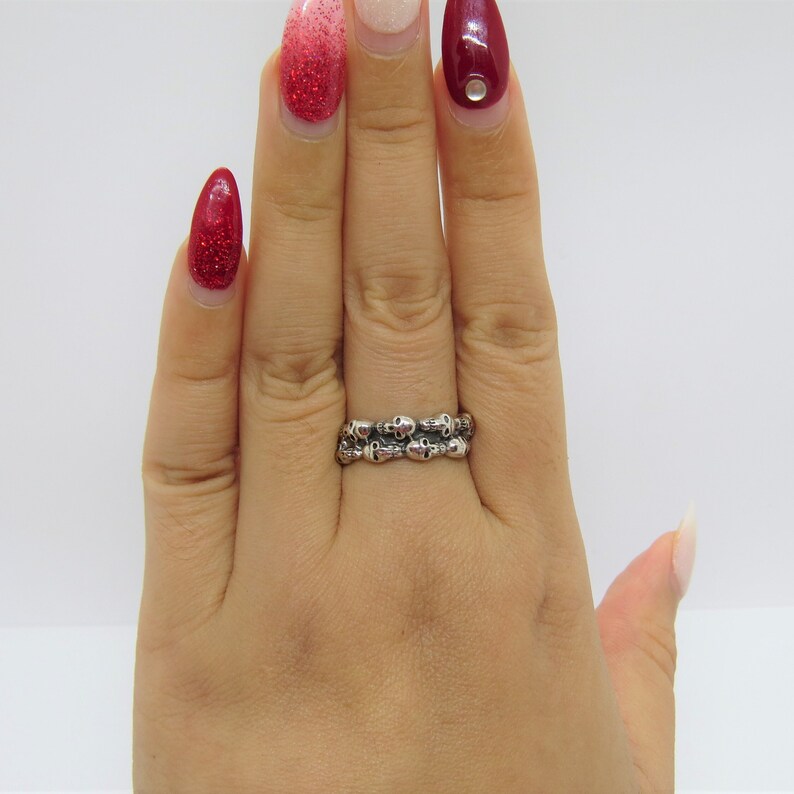 May include: A silver ring with a double row of skull designs. The ring is worn on a person's finger.