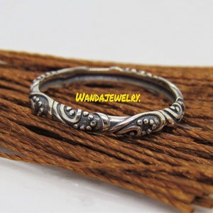 May include: A silver ring with an intricate, swirling design. The ring is thin and delicate, with a smooth finish. The design features a series of small dots and curves.
