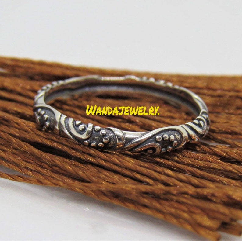 May include: A silver ring with an intricate, swirling design. The ring is thin and delicate, with a smooth finish. The design features a series of small dots and curves.