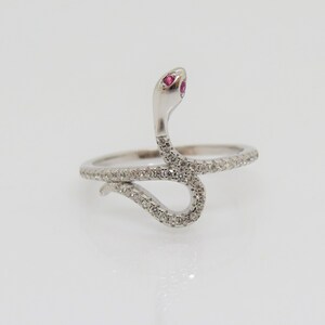 May include: A silver-toned snake ring with a raised head and a curved body. The snake's eyes are small, red gemstones. The body of the snake and the ring band are encrusted with small, clear gemstones.