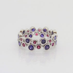May include: A silver ring with a double row of purple and pink gemstones. The ring is made of a silver band with a series of small, round gemstones set in a circle.