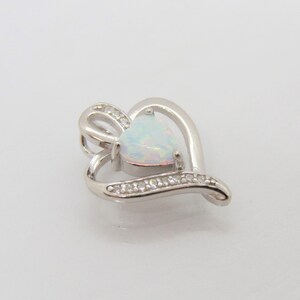 May include: A silver heart-shaped pendant with a white opal gemstone in the center. The pendant is accented with small clear stones around the edge.
